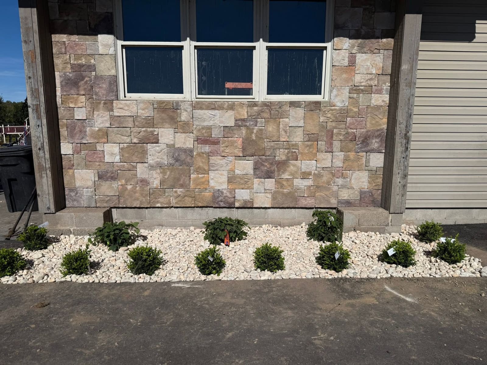 Fresh foundation planting with white stone and new shrubs against a stone house wall