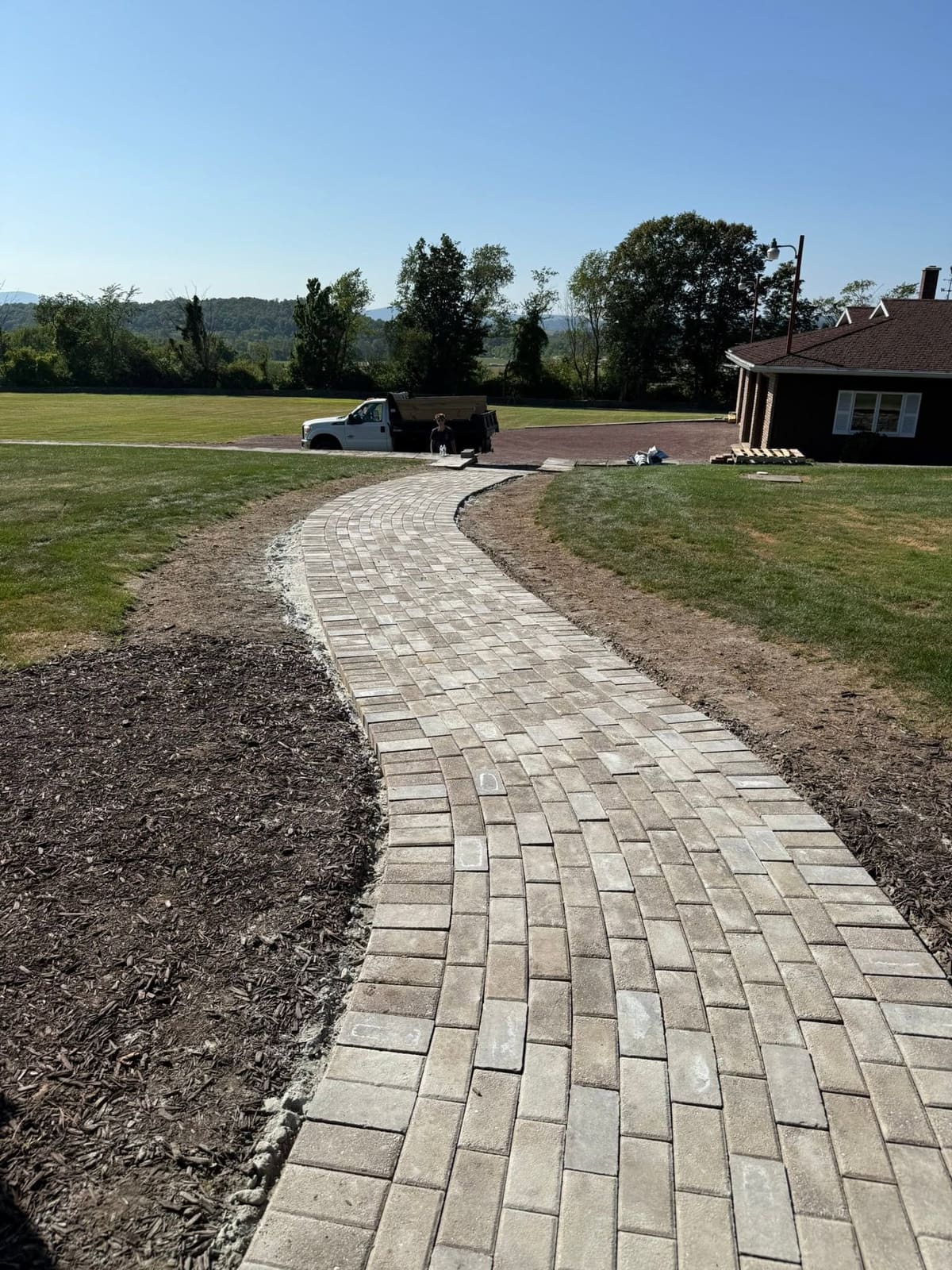 New curved paver walkway leading to a home with fresh grading on both sides