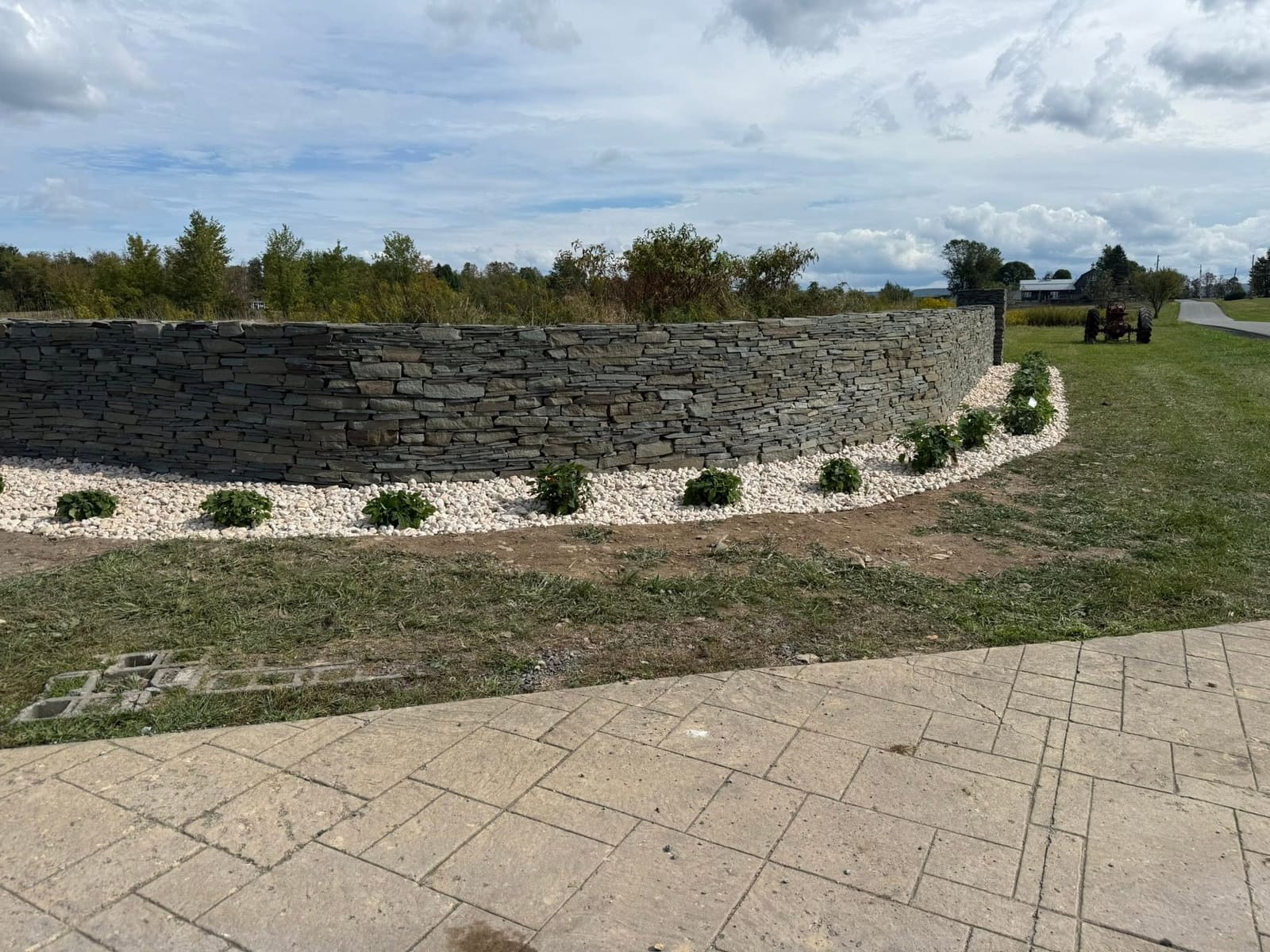 Long curved stacked-stone retaining wall with fresh white gravel beds and new shrubs